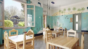 A room with wooden furniture, a window with a view of greenery, and wall decorations including fish and palm trees.