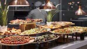 Un bufé con diversos platos, entre ellos ensaladas, pizzas y aperitivos, expuestos sobre pedestales de madera.