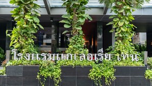 A building entrance with a sign in a foreign script, surrounded by lush greenery and modern architecture. - Galleria 10 Hotel Bangkok (Bangkok)