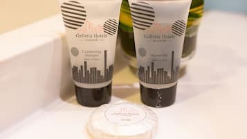 Two toiletry tubes labeled 'Galleria Hotels Bangkok' on a white surface, with a vase of orange flowers in the background.