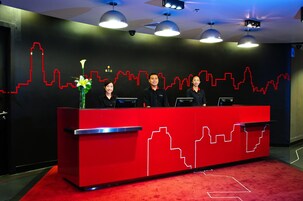Een receptiebalie met een rood en zwart design, drie medewerkers en een stadsgezicht op de muur.