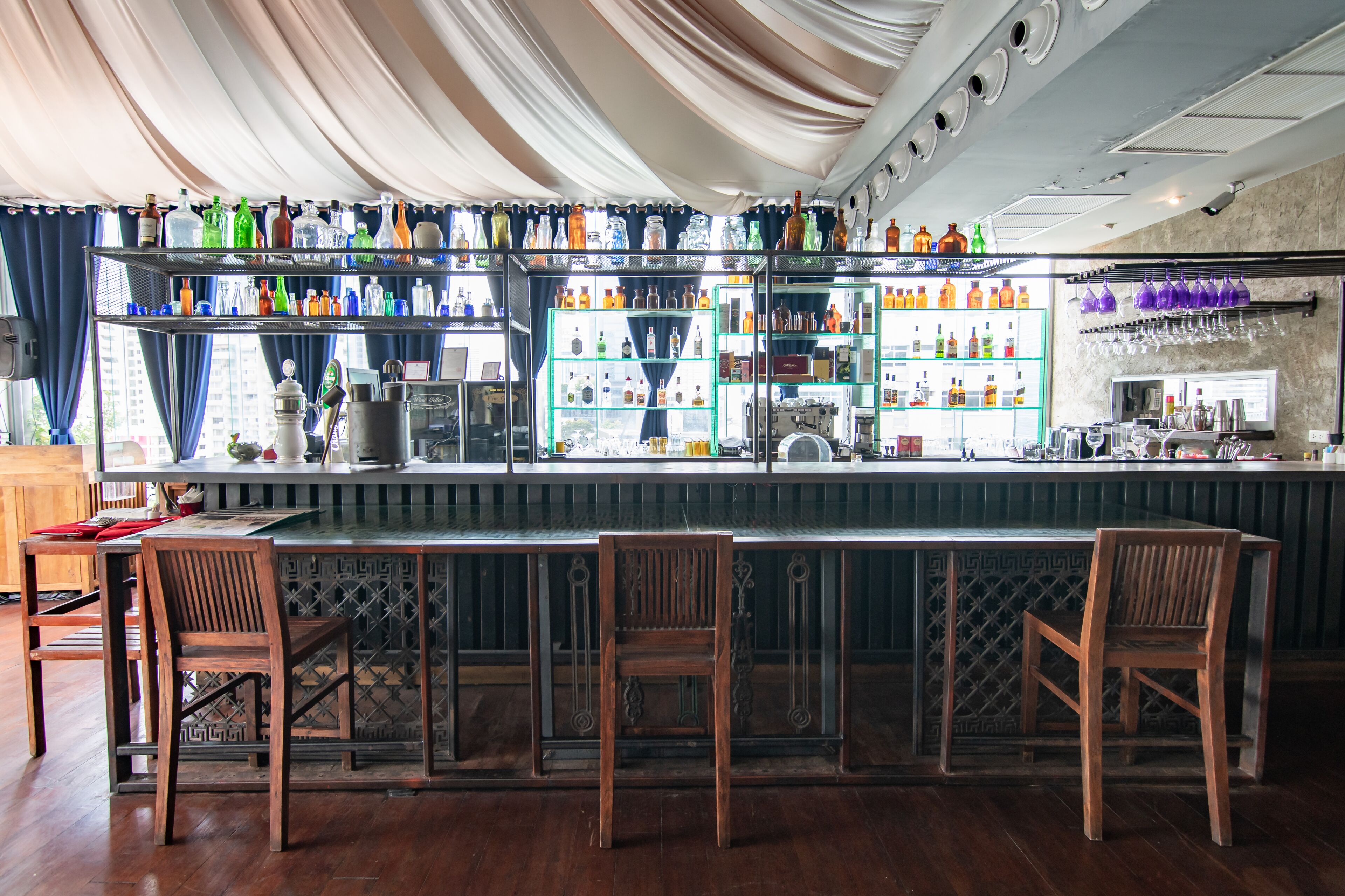 A bar area with wooden chairs, a counter, and shelves stocked with bottles.