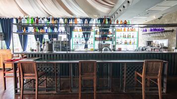 A bar area with wooden chairs, a counter, and shelves stocked with bottles.