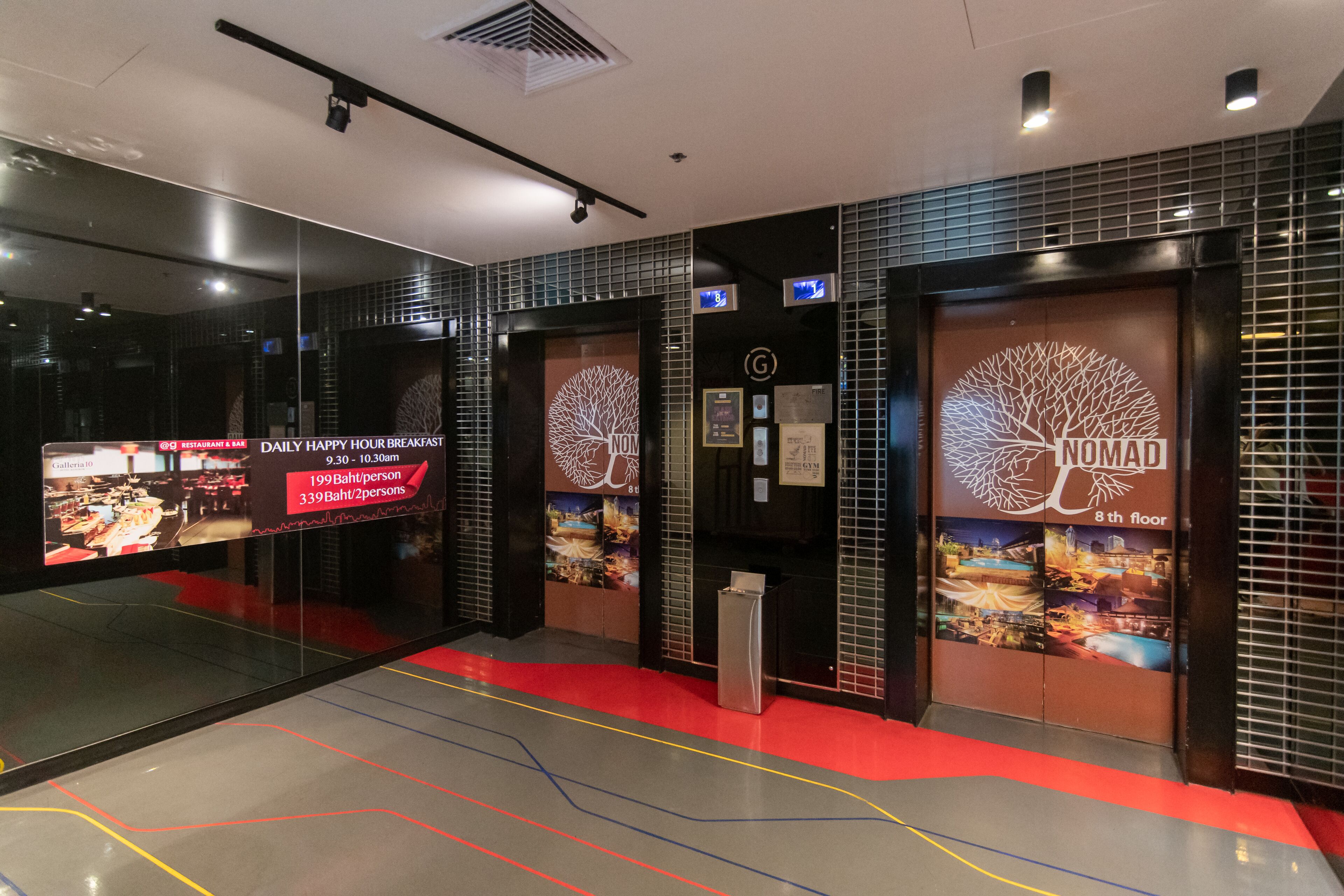 A hotel lobby with a red carpet, a digital clock, and a sign for 'Daily Happy Hour Breakfast'.