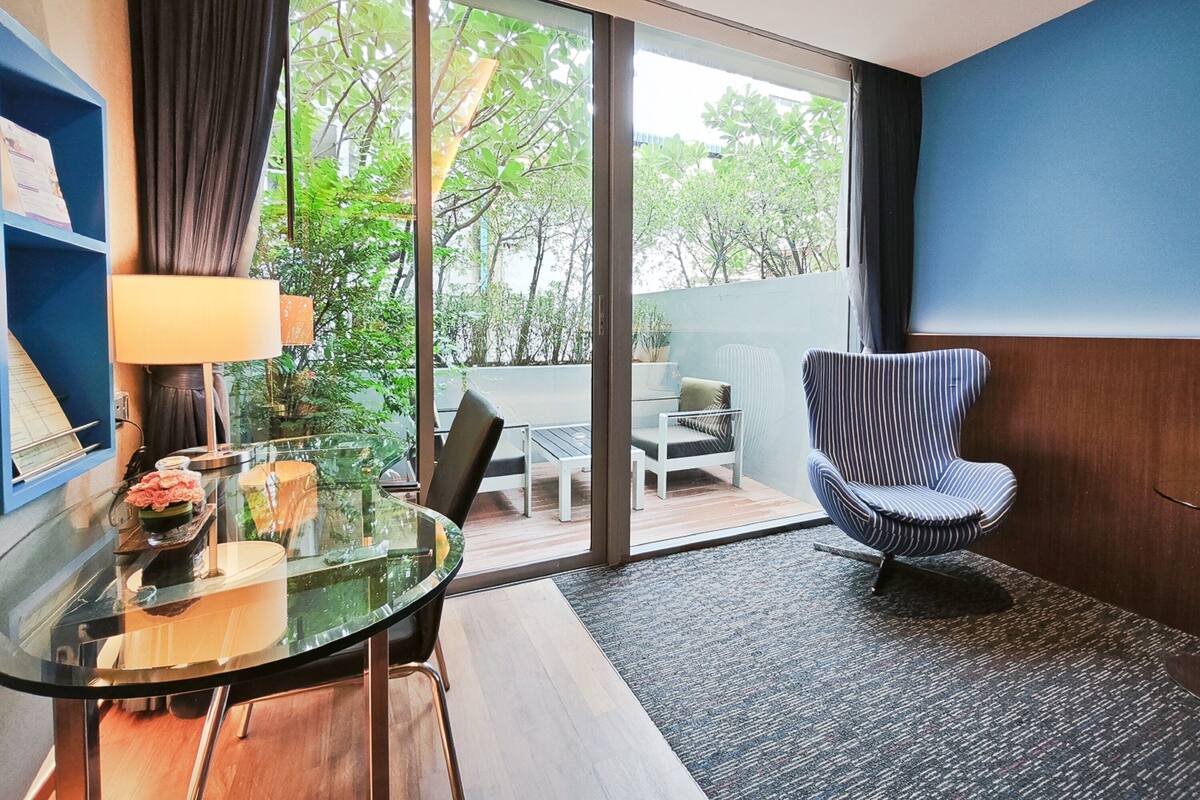 A modern room with a glass table, chairs, a lamp, and a view of greenery outside.