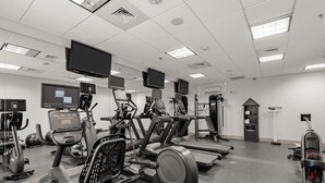 A gym with various exercise machines, a large mirror, and multiple screens.