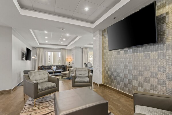 A modern living room with a flat-screen TV mounted on the wall, comfortable seating, and a patterned wall. - Holiday Inn Express & Suites Gonzales by IHG (Gonzales)