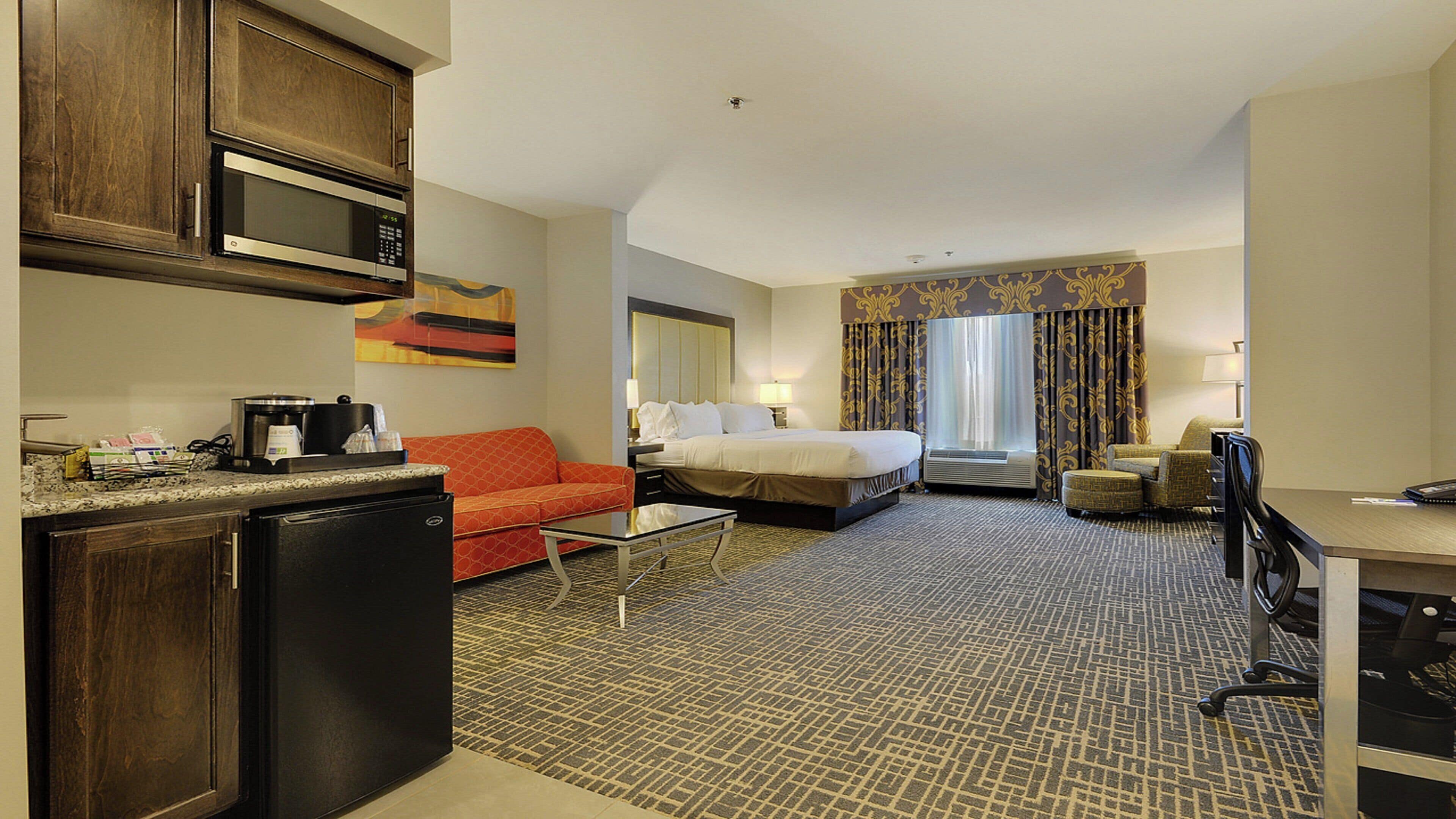 A hotel room with a kitchenette, a bed, a sofa, a desk, and a bathroom.