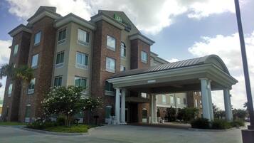 A multi-story hotel with a brick facade, a covered entrance, and a landscaped area with trees and shrubs.