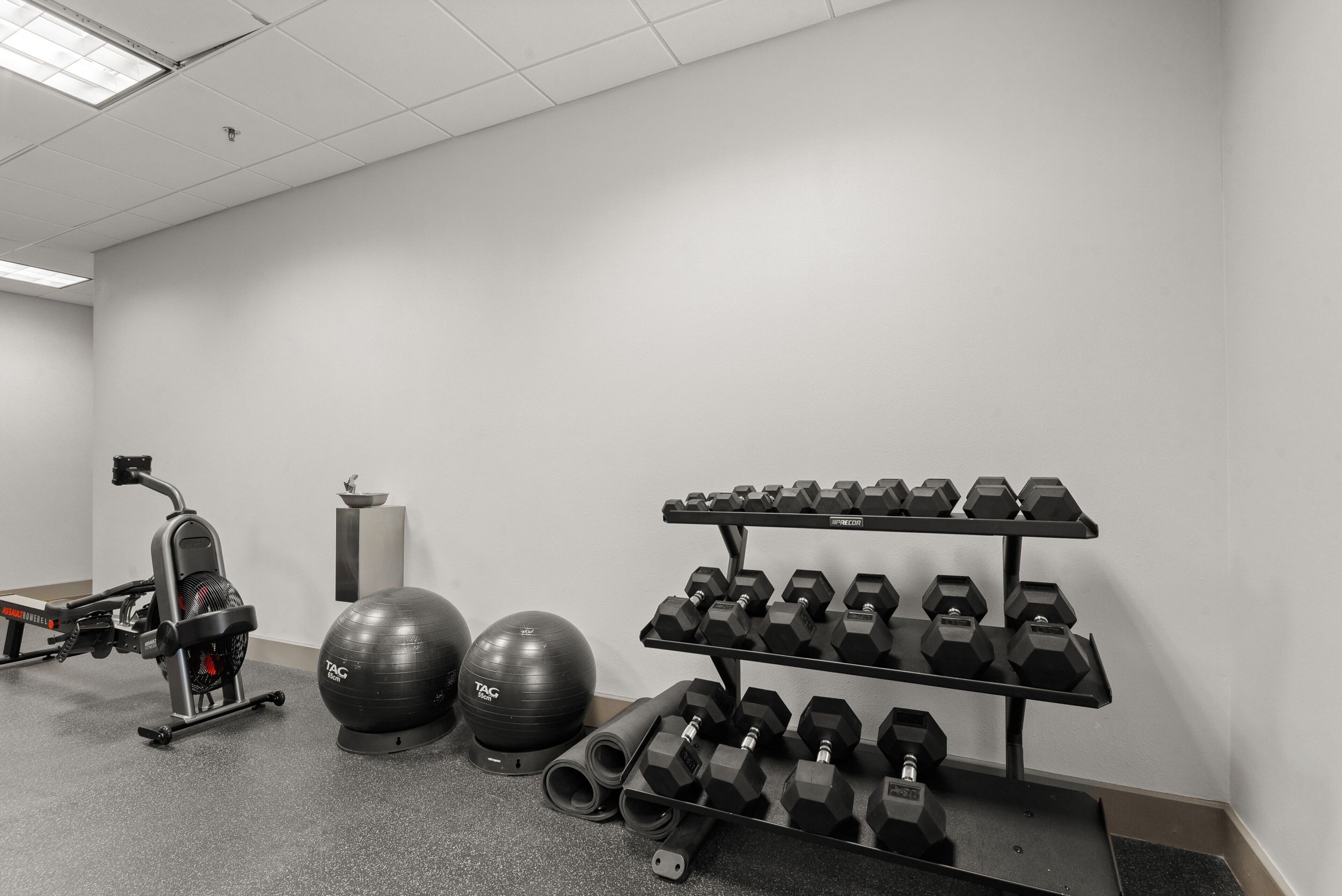 A gym with exercise equipment including a stationary bike, dumbbells, and exercise balls.