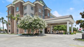 A hotel with a brick facade, a covered entrance, and a landscaped area with flowering trees.