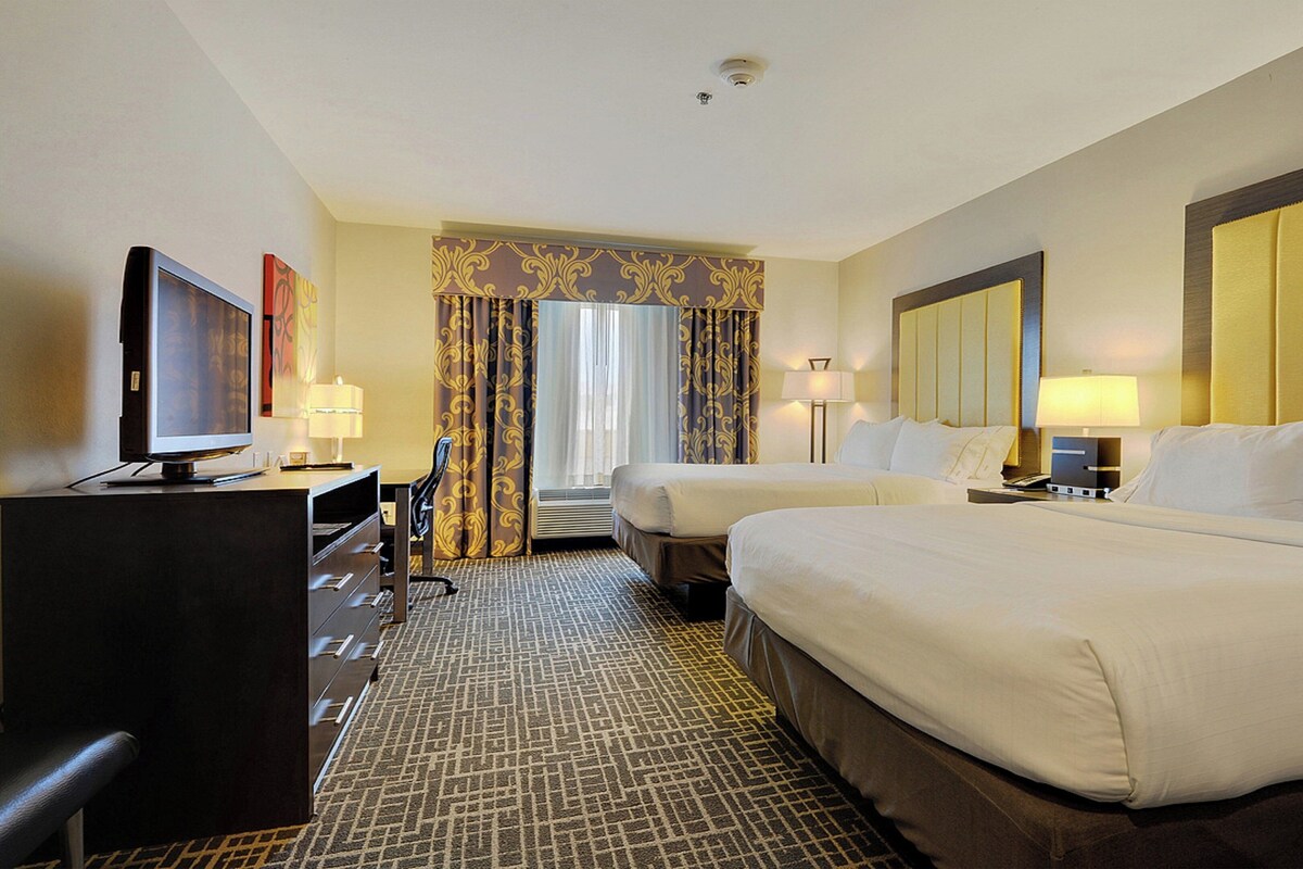 A hotel room with two beds, a desk with a computer, a television, and a window with curtains.