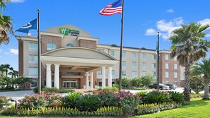 A Holiday Inn Express hotel with a covered entrance, flagpoles, and landscaped gardens. - Holiday Inn Express & Suites Gonzales by IHG (Gonzales)