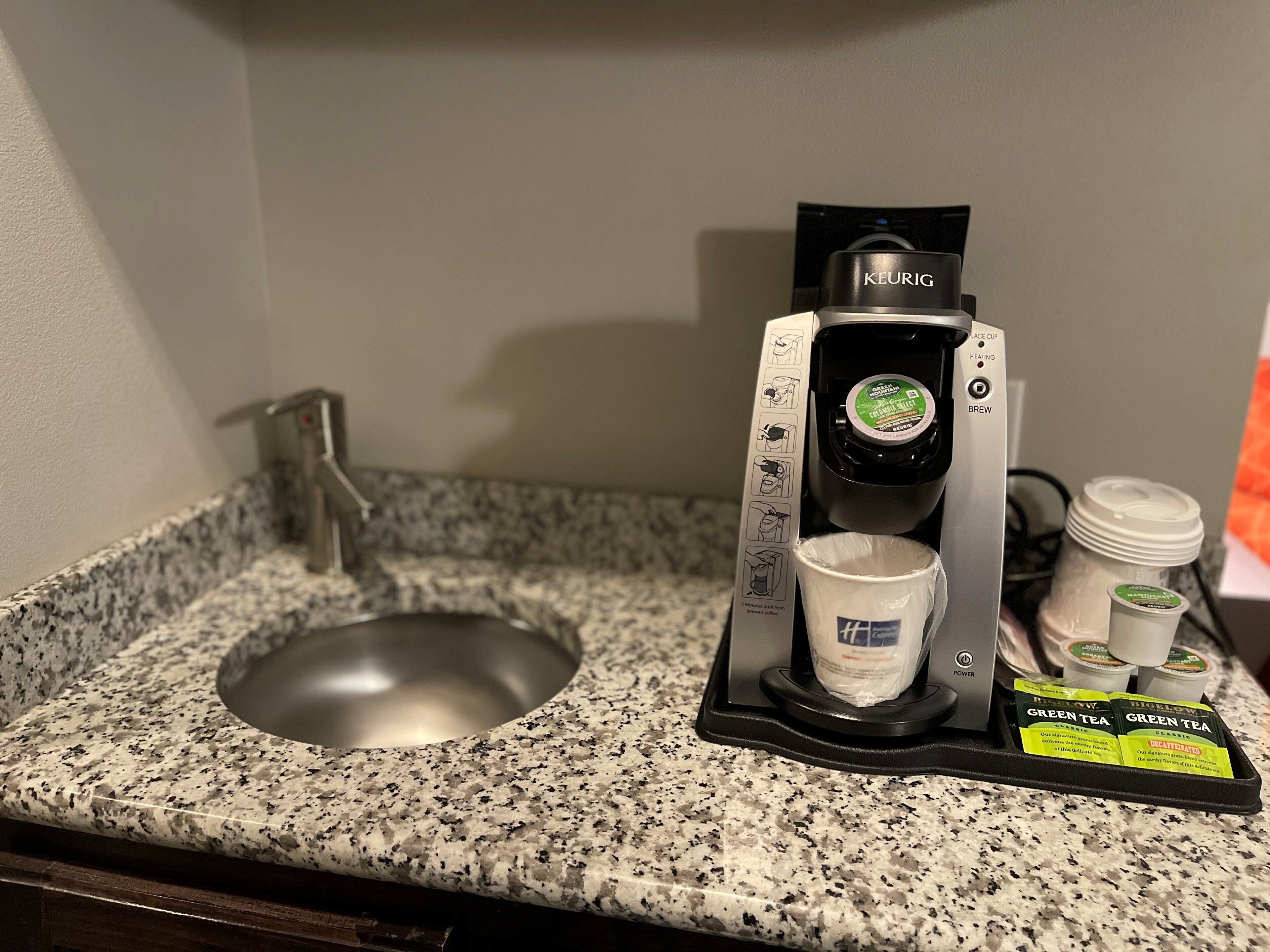 Una cafetera Keurig con una bandeja de goteo, un lavamanos y una encimera.