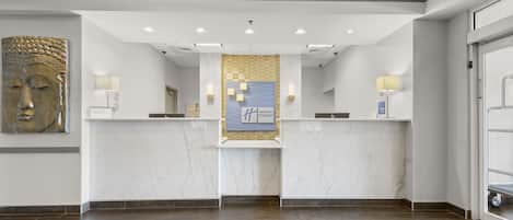 Zona de recepción de un hotel con mostradores de mármol, una gran escultura en la pared y un cartel de Holiday Inn Express.