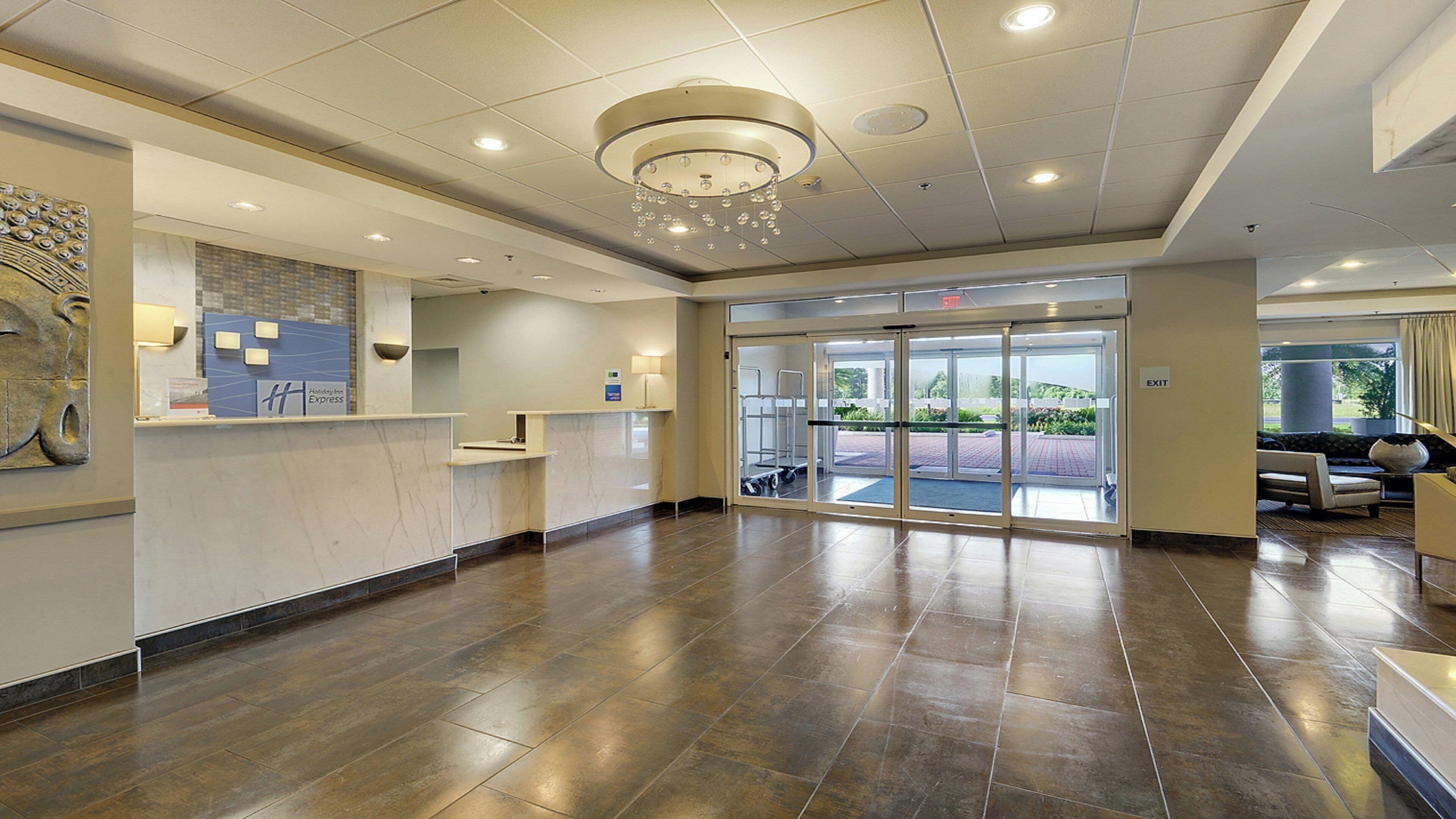A hotel reception area with a marble counter, a chandelier, and a glass door entrance.