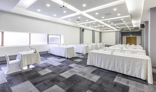 A conference room with multiple tables set for a meeting, equipped with microphones and glassware.