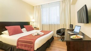 Habitación de hotel con cama, escritorio, laptop, televisor de pantalla plana y ventana con cortinas.