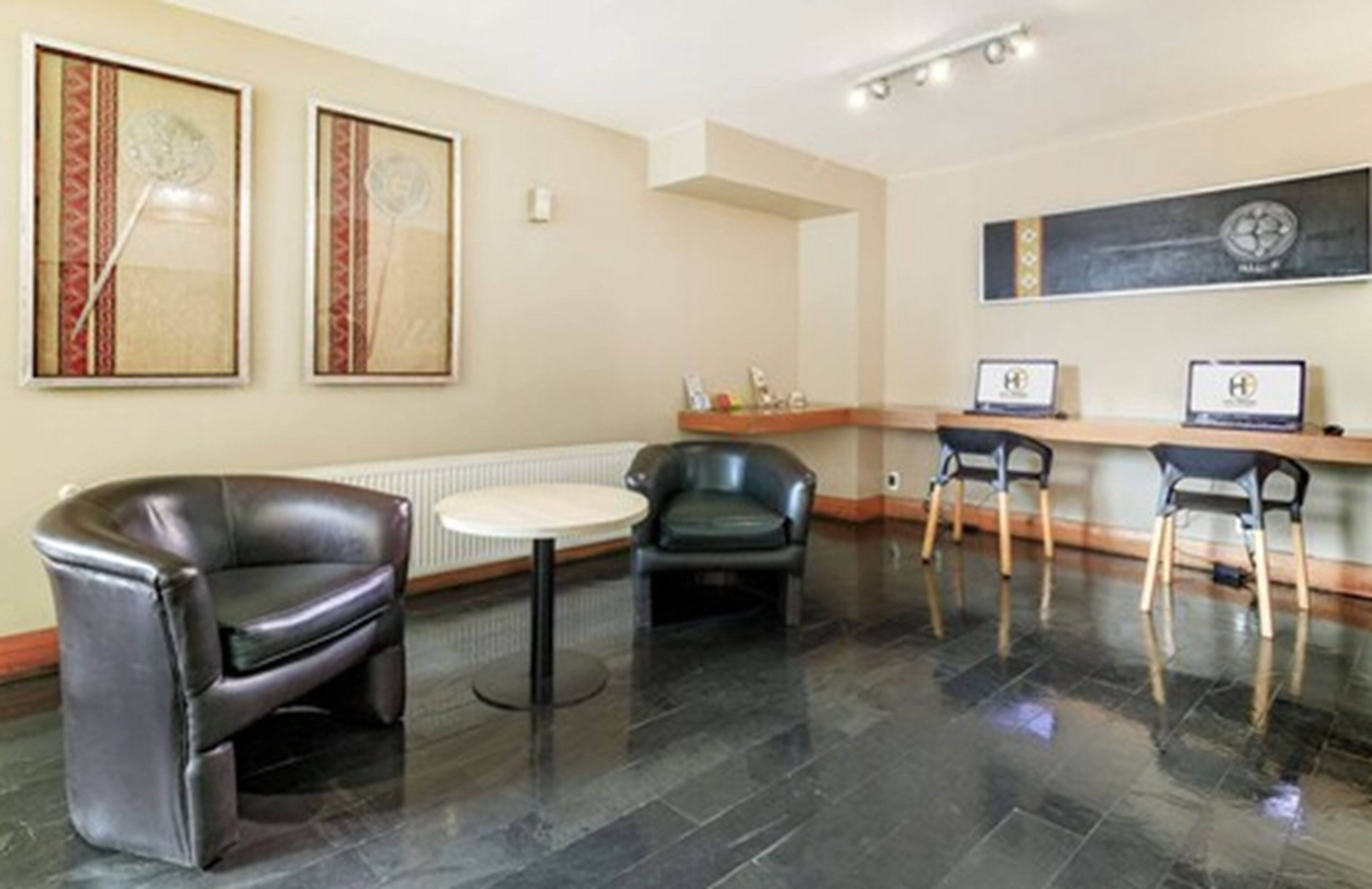 Een hal met lederen stoelen, een klein rond tafeltje en kunstwerken in lijsten aan de muren.