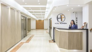 Zona de recepción de un hotel con diseño moderno, que incluye un mostrador de recepción, un logotipo grande en la pared y un largo pasillo con puertas a la izquierda.