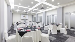 Un salón de conferencias con mesas redondas, sillas blancas y una pantalla proyectora mostrando el logotipo del hotel.