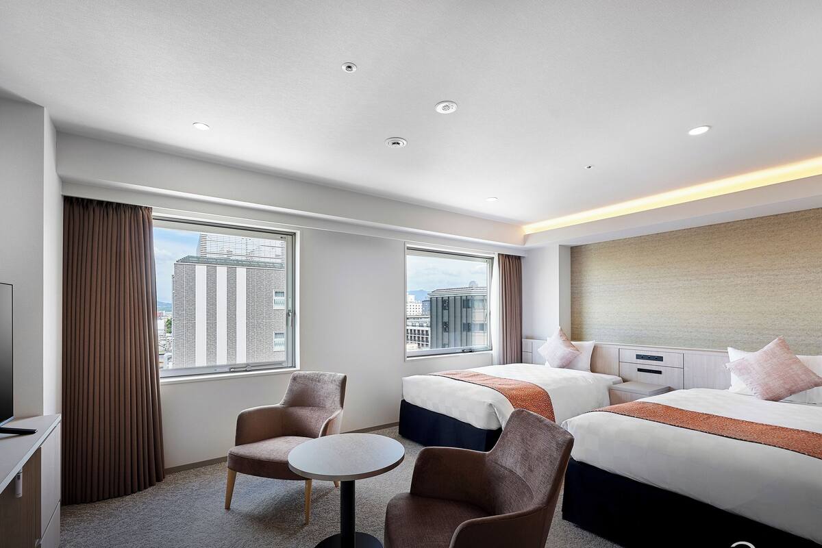 Ein Hotelzimmer mit einem Bett, zwei Sesseln, einem kleinen Tisch und einem Fernseher.