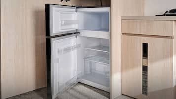 A compact refrigerator with a freezer compartment on top, a main compartment below, and a transparent storage drawer.