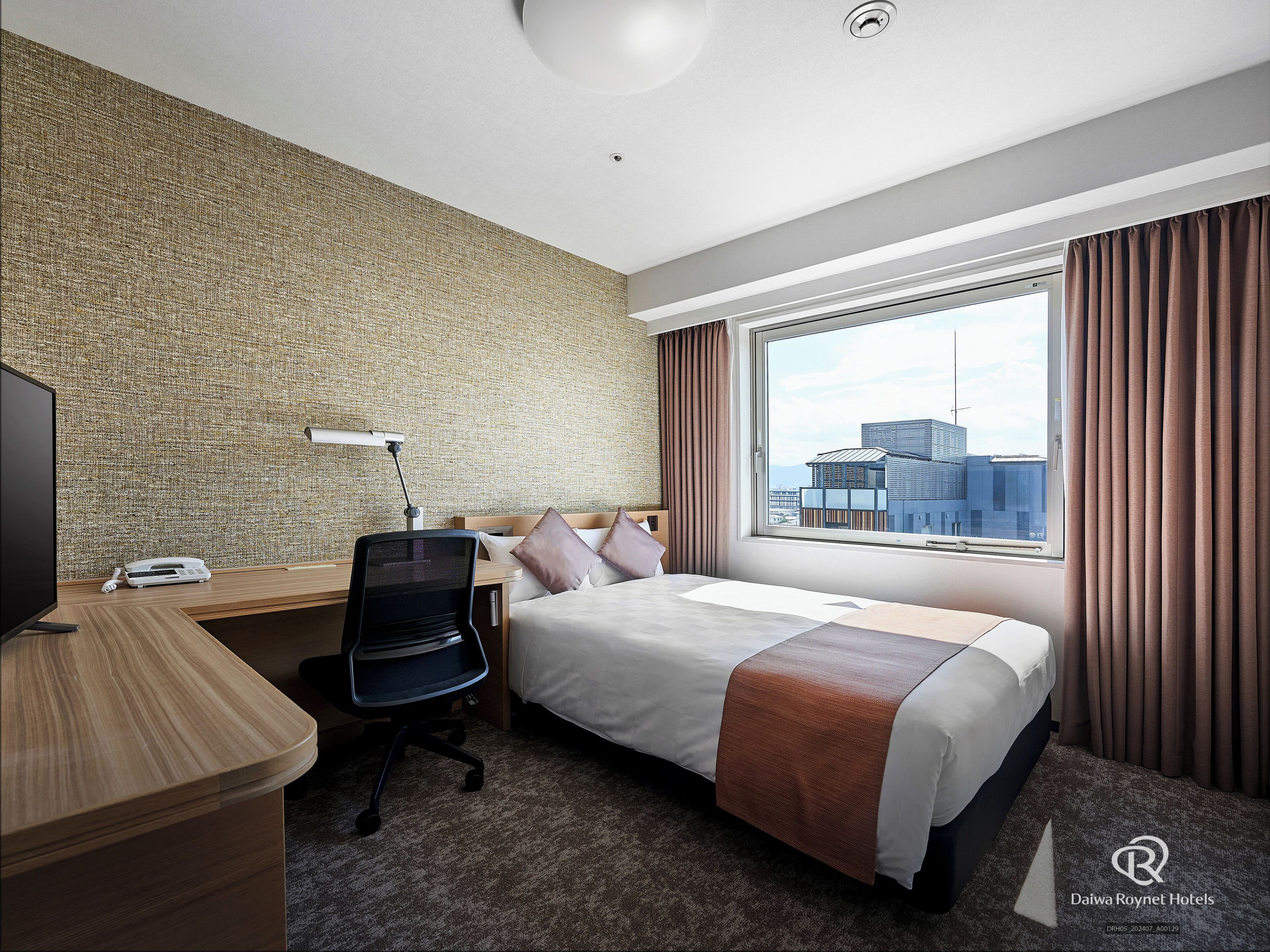 Ein Hotelzimmer mit Bett, Schreibtisch, Stuhl und einem großen Fenster mit Vorhängen.
