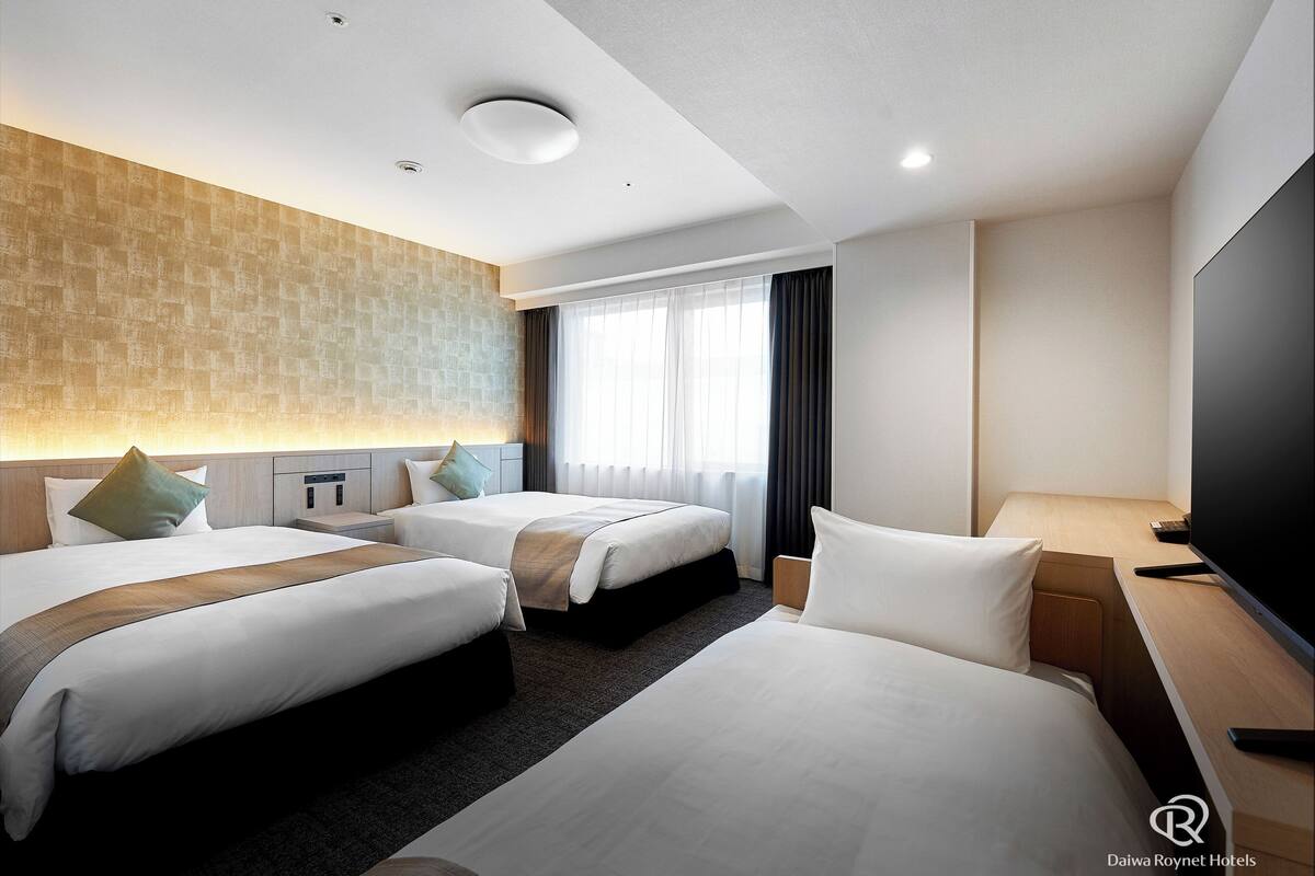 Ein Hotelzimmer mit zwei Betten, einem Flachbildfernseher, einem Schreibtisch und einem großen Fenster mit Vorhängen.