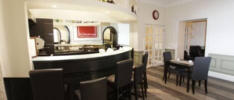 A bar area with a counter, bar stools, and a dining table with chairs. There are bottles on the counter and a clock on the wall.