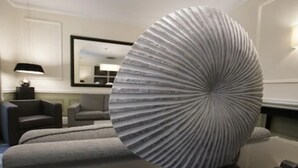 Una sala de estar moderna con una gran escultura circular acanalada sobre una mesa, un sofá y una lámpara.
