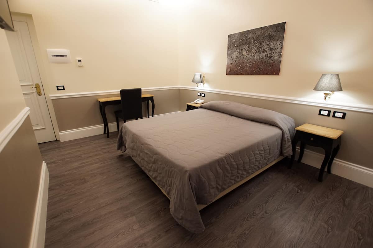 Une chambre d’hôtel avec un lit, un bureau, une chaise, deux tables de chevet, une lampe et un tableau au mur.