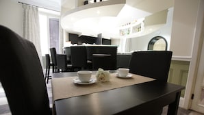 Un comedor con una mesa dispuesta para dos, una rosa blanca y un bar al fondo.