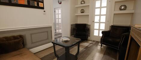 Uma sala de estar com um sofá, duas poltronas, uma mesa de centro e prateleiras decorativas.