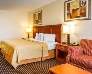 A hotel room with a large bed, a wooden headboard, two bedside tables with lamps, a checkered armchair, and a striped carpet.