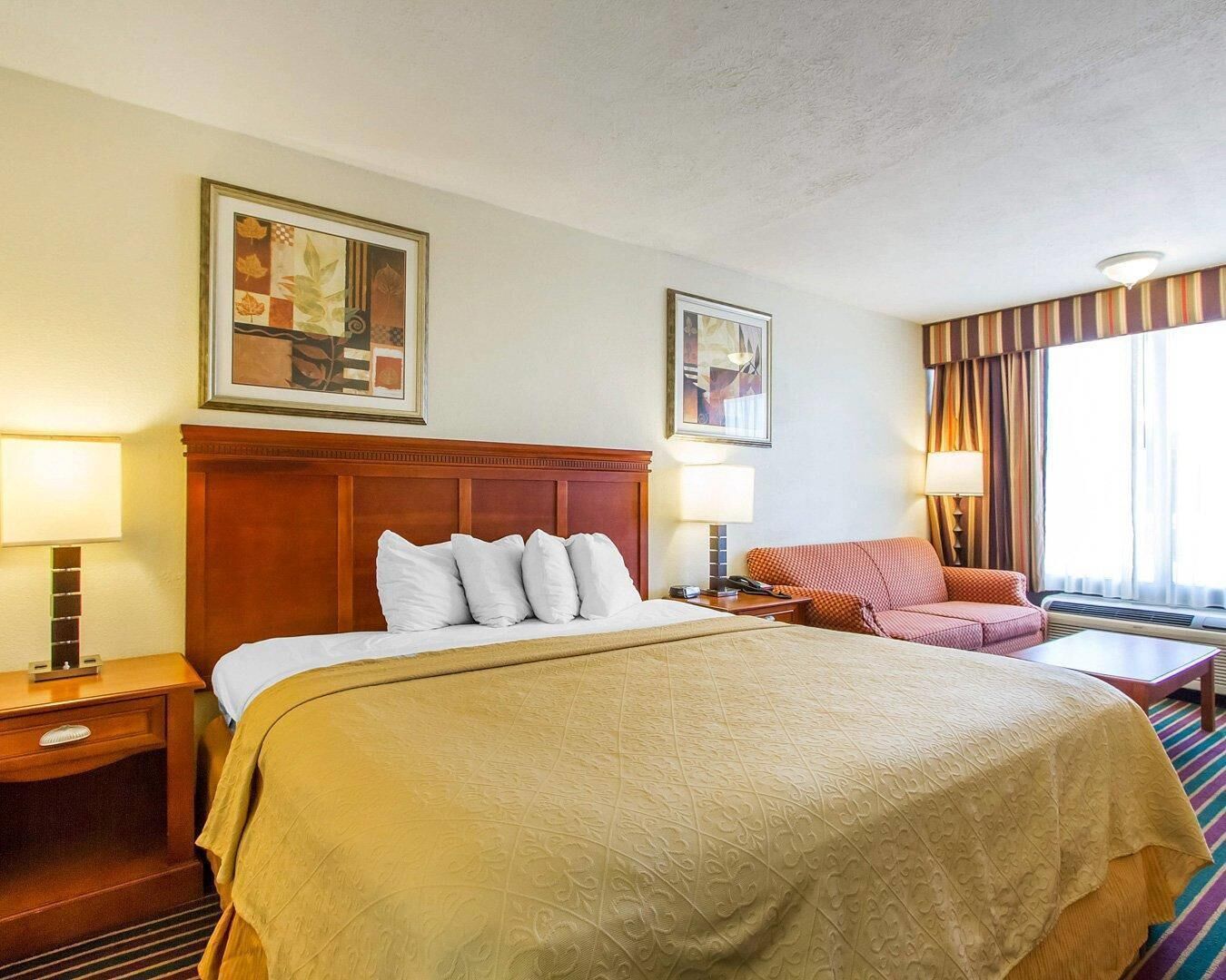 Une chambre d’hôtel avec un grand lit, deux tables de chevet, une chaise et une fenêtre avec des rideaux.