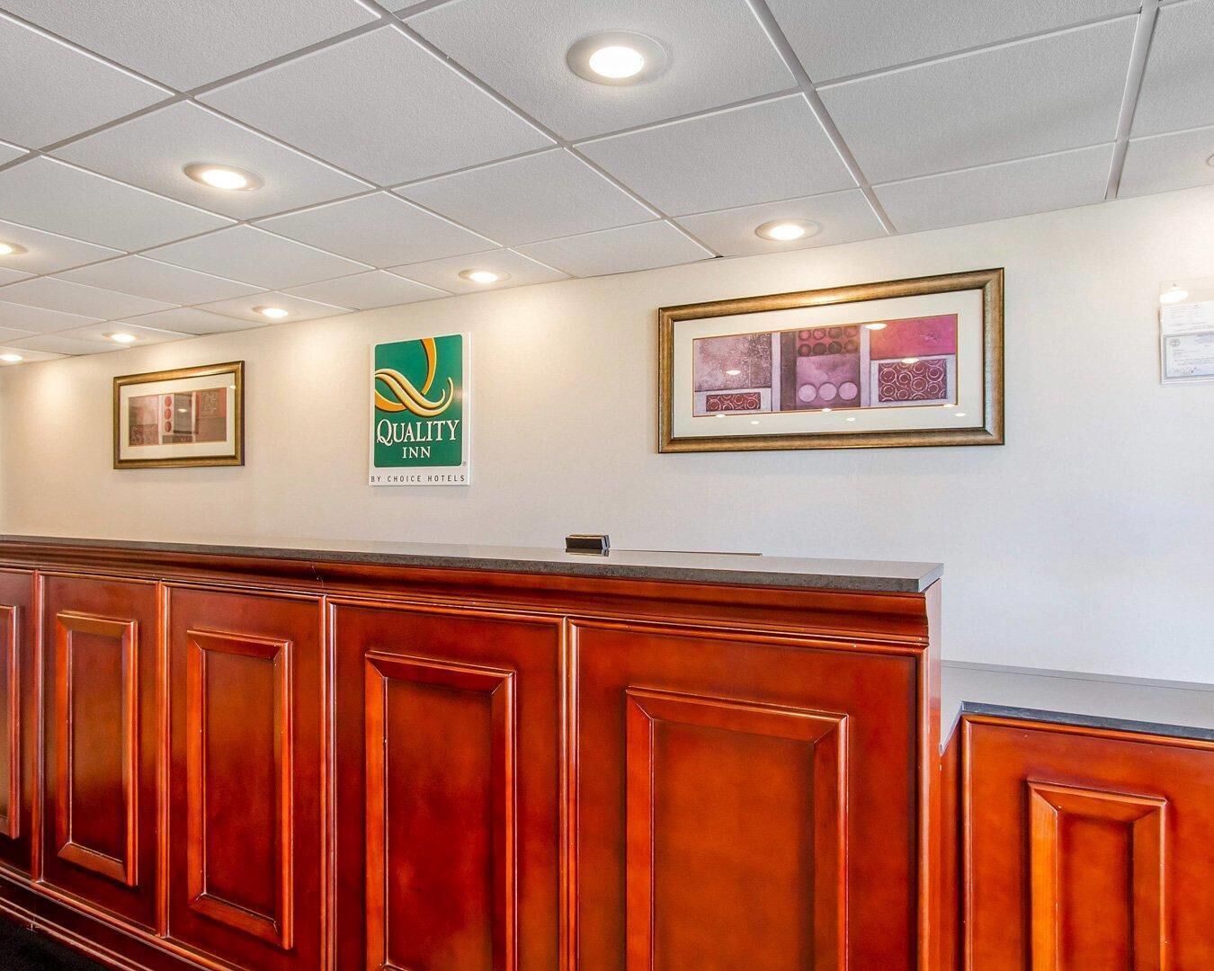 Zona de recepción de un hotel con un mostrador de madera, una obra de arte enmarcada en la pared y un cartel de Quality Inn.