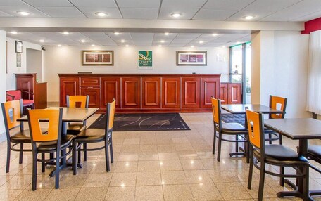 A hotel dining area with multiple tables and chairs, a reception desk, and a logo on the wall.