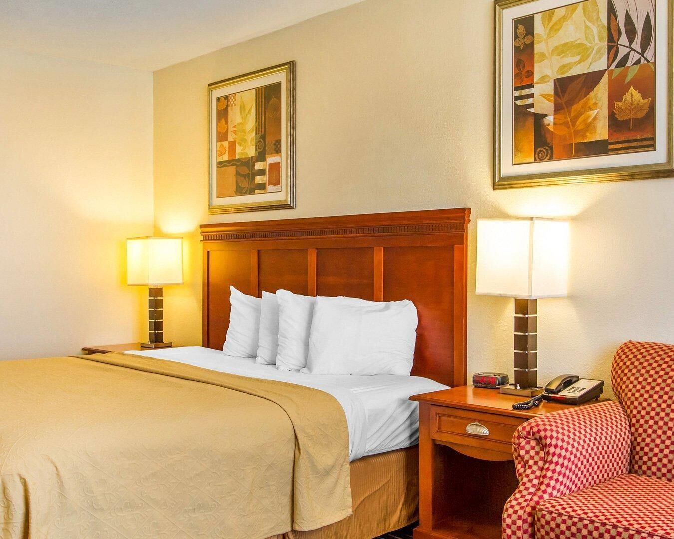 Habitación de hotel con una cama, dos mesitas de noche, una silla y dos lámparas de pared.