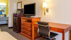 Ein Hotelzimmer mit einem Holztisch, einem Fernseher, einer Lampe, einer Kommode und einem Streifen Teppich.