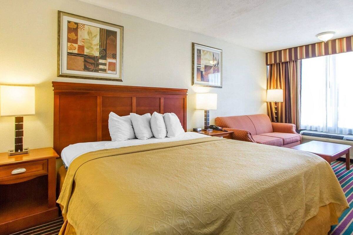 A hotel room with a large bed, two bedside tables, a chair, a desk, and a window with curtains.