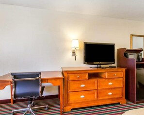A hotel room with a wooden desk, a black office chair, a television, a lamp, and a microwave.
