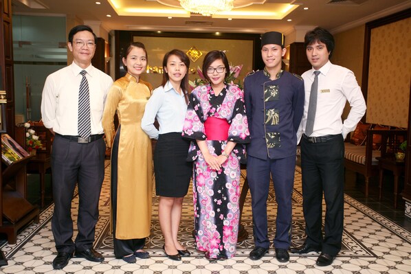 A group of people standing in a room with a patterned floor and a chandelier.