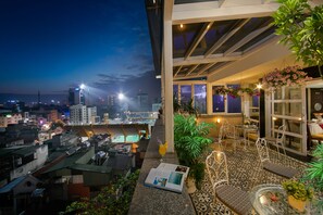 A rooftop terrace with seating, a magazine, and a view of the city skyline at night. - Hanoi Emotion Hotel (Hanoi)