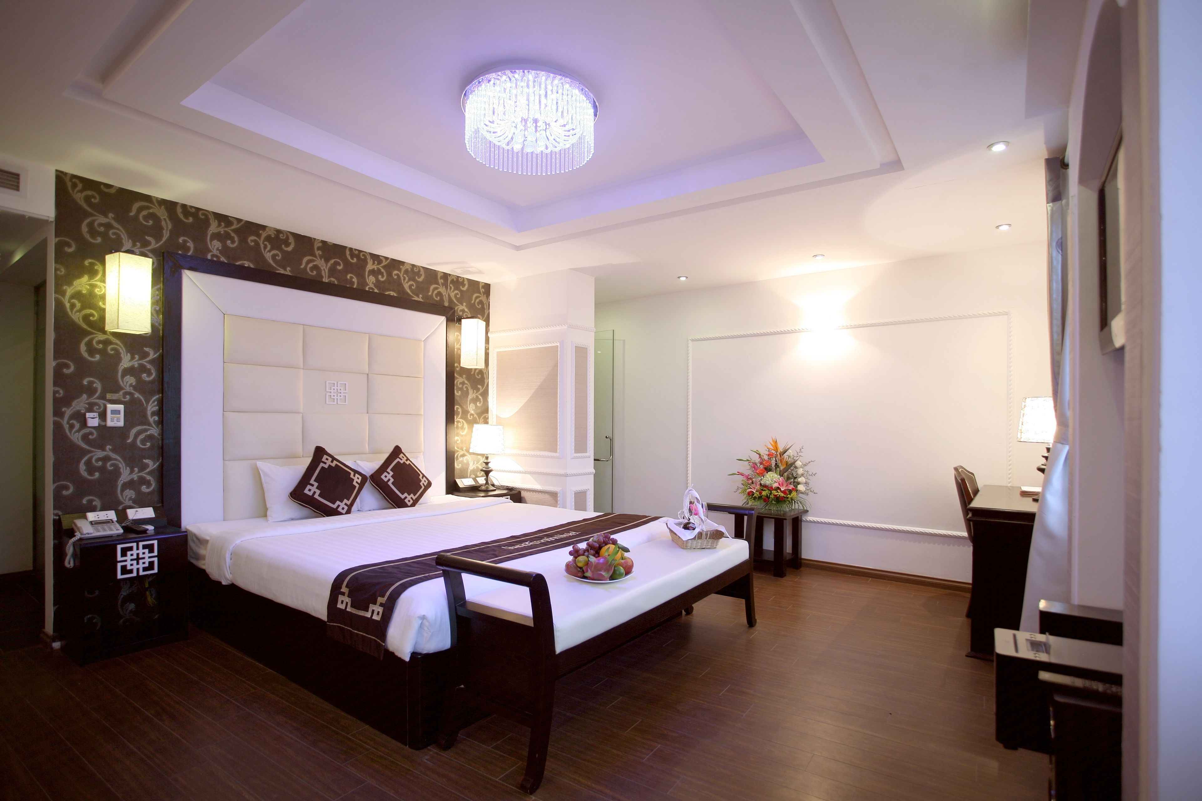 A hotel room with a large bed, bedside tables, a desk, and a chandelier.