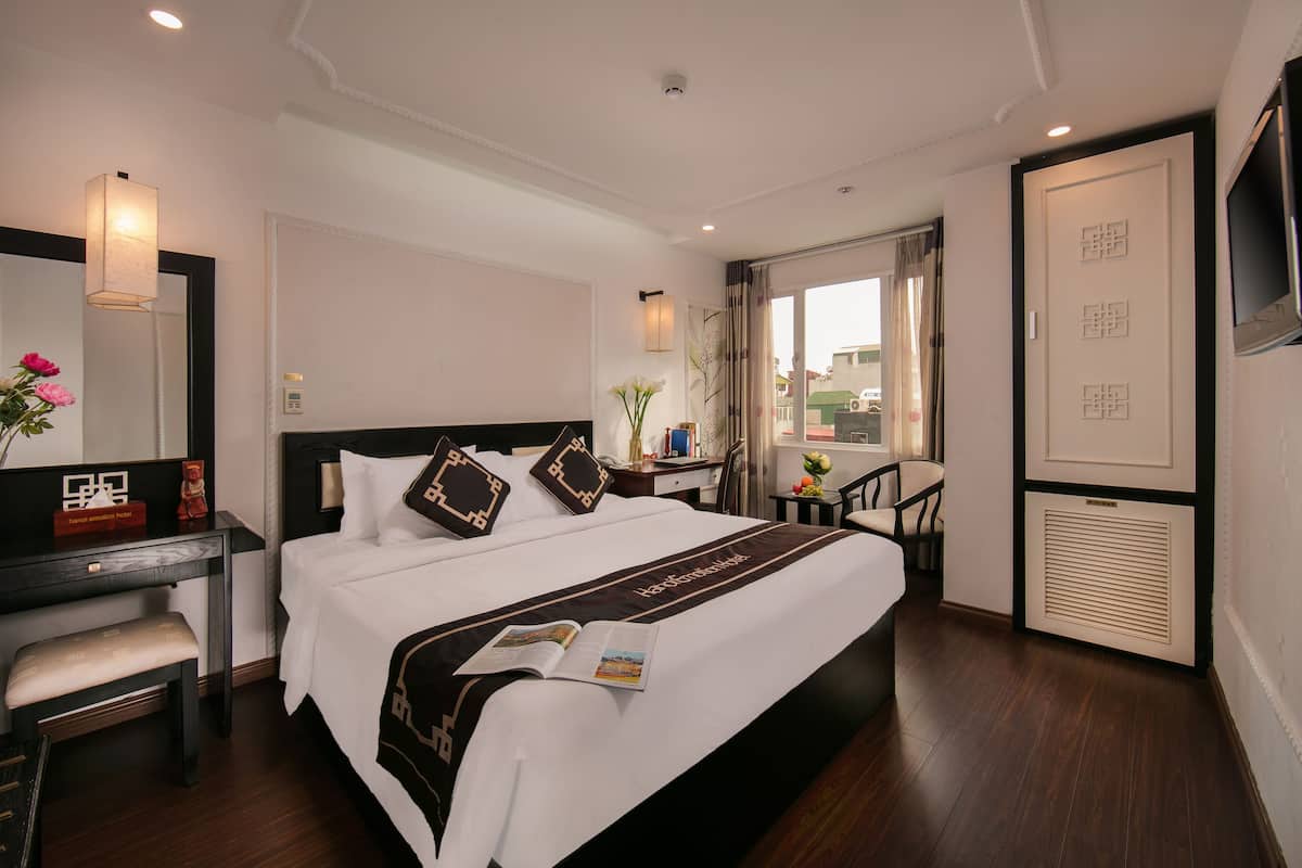 Une chambre d’hôtel avec un grand lit, un bureau avec une chaise, une télévision et une fenêtre avec des rideaux.