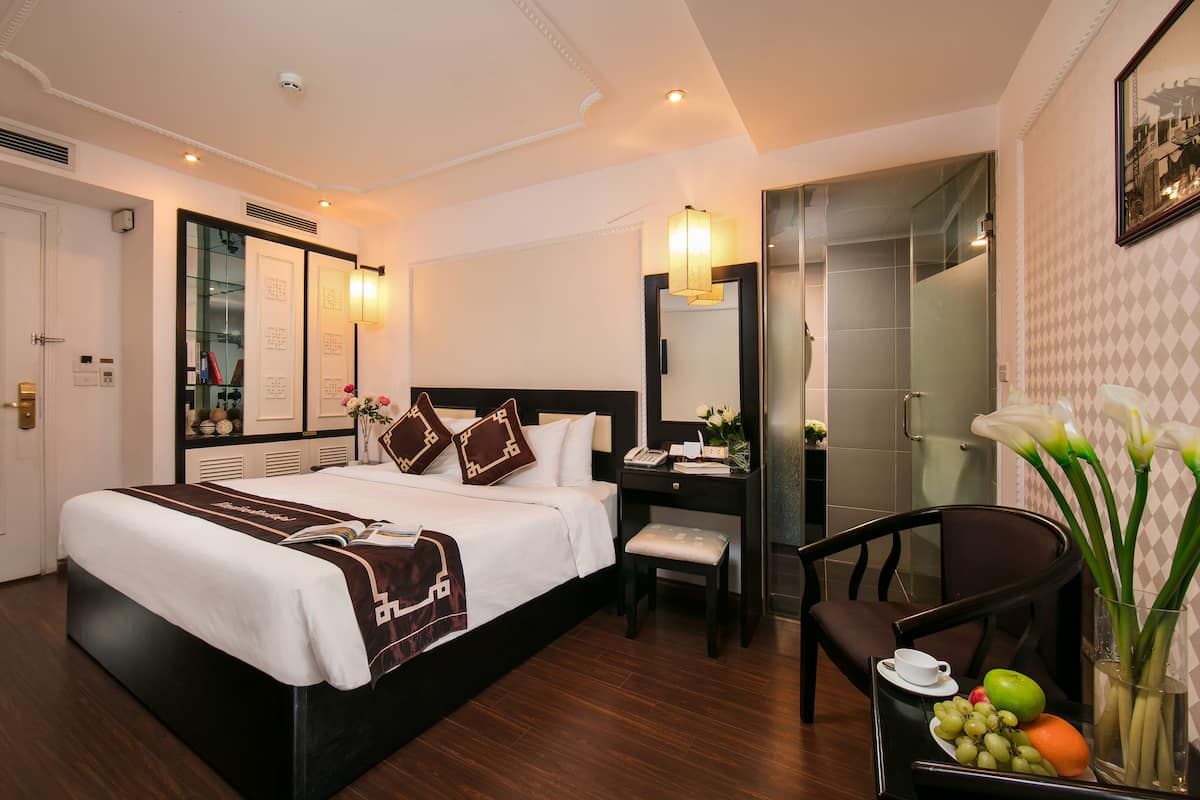 Une chambre d’hôtel avec un grand lit, une table de chevet, une chaise et un bureau avec une lampe.