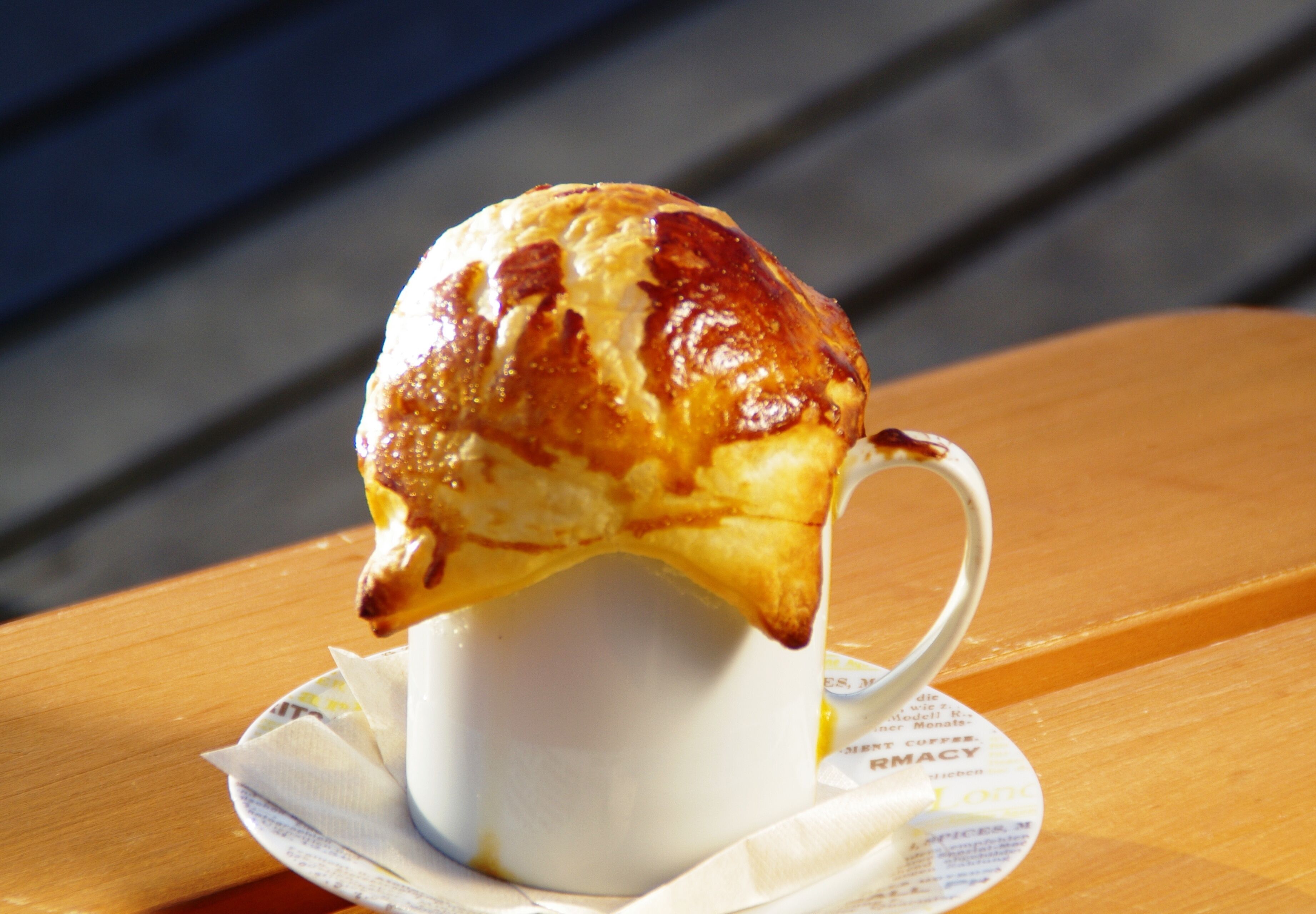 A cup of coffee with a pastry on top, placed on a wooden table with a napkin underneath.