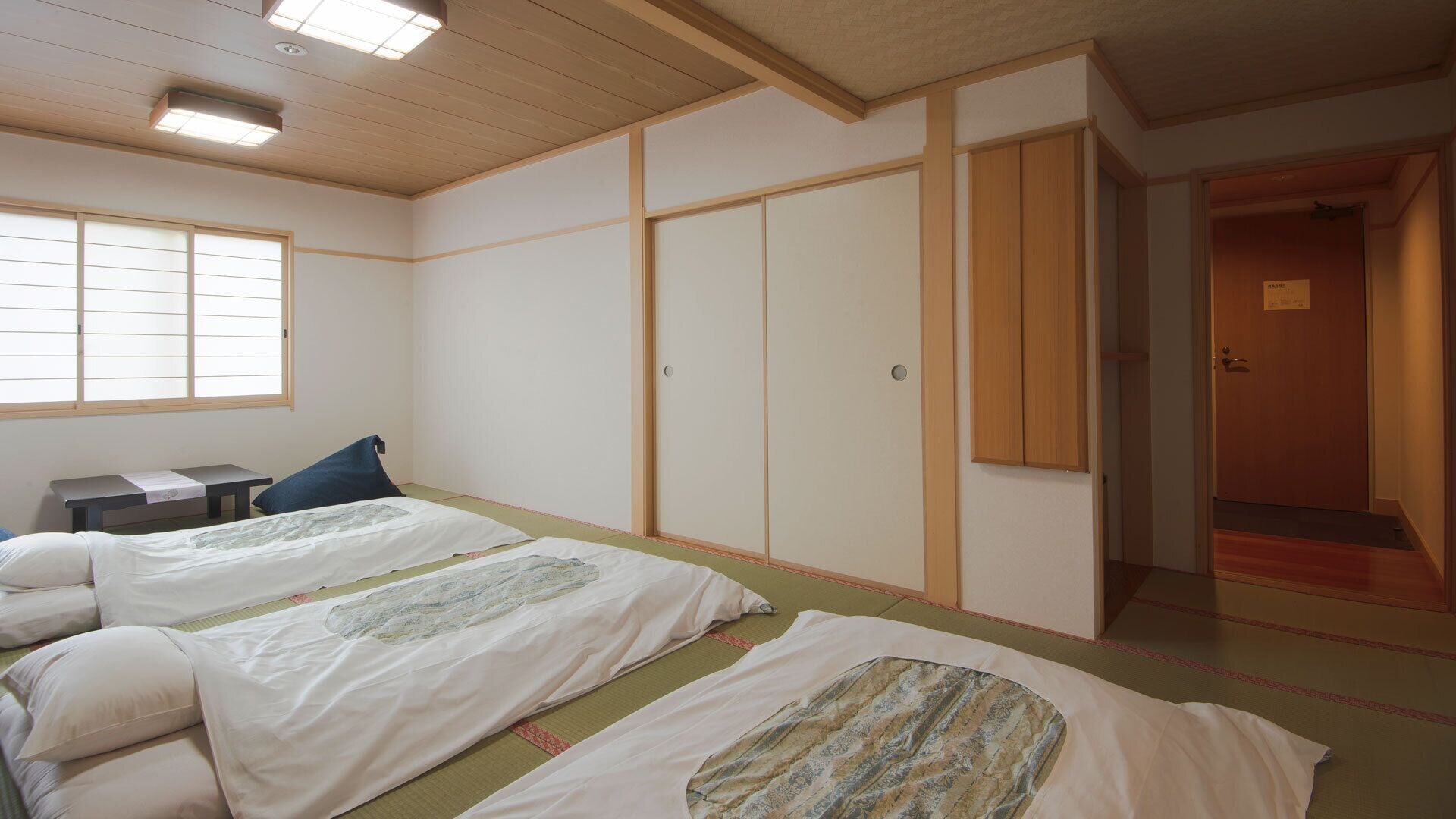 A traditional Japanese-style room with tatami flooring, two beds with white bedding, a small table, and sliding doors.
