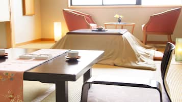 Una habitación tradicional japonesa con suelo de tatami, una mesa baja con camino de mesa, dos sillas y una mesa pequeña con un jarrón de flores.